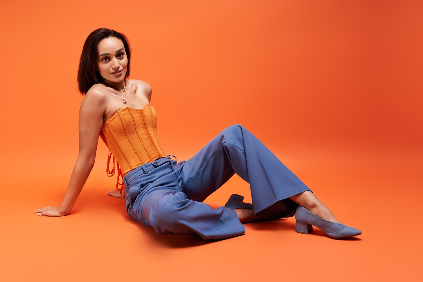 Model in an orange corset and blue trousers striking an editorial pose