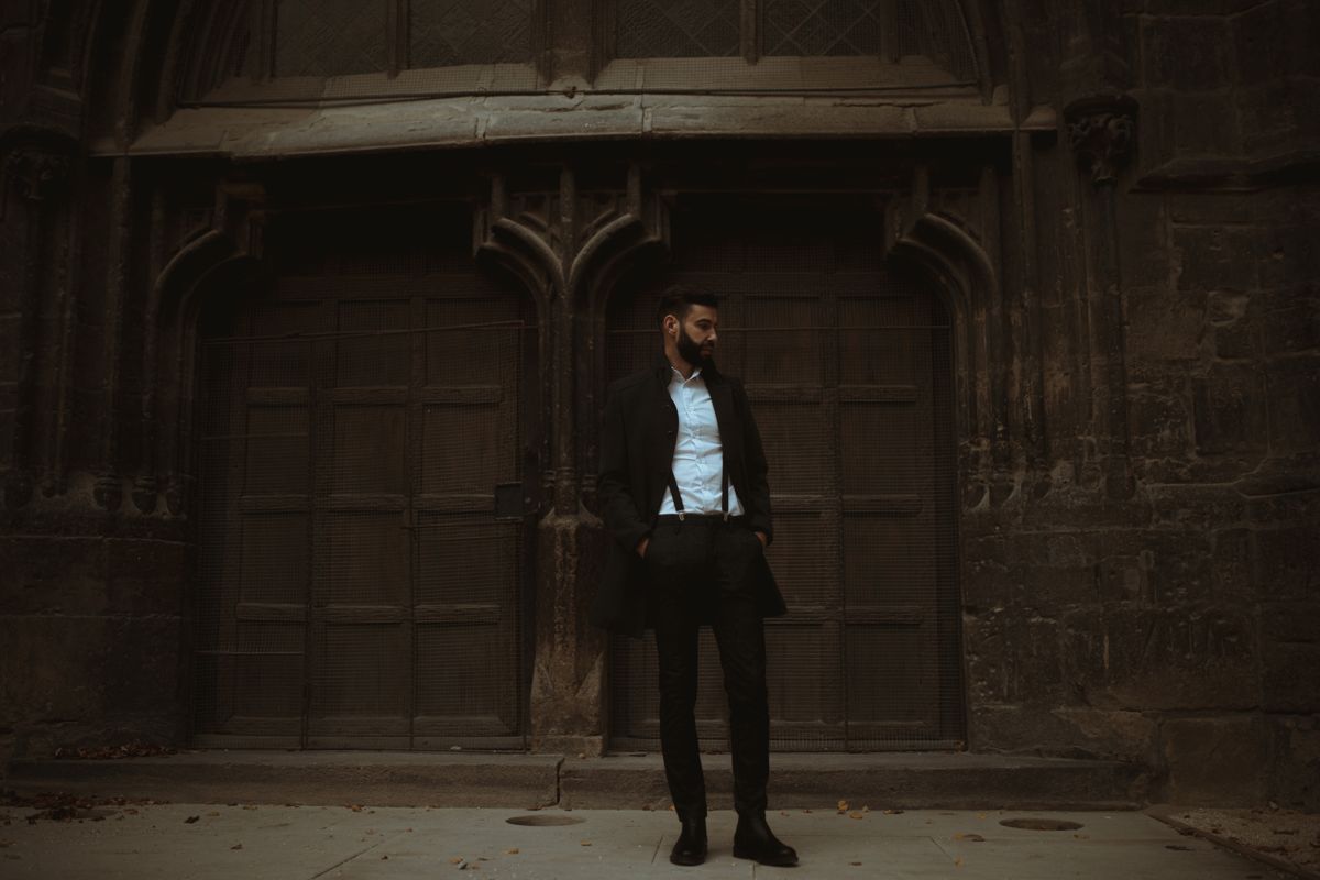 Bearded man in dark tailored suit standing before gothic architecture